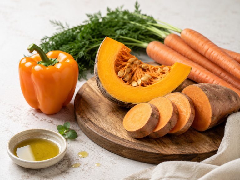 морковь, тыква, батат и оранжевый перец на светлом фоне, рядом капля оливкового масла и деревянная доска